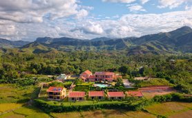 Eine malerische Ansicht des Ranomafana Hotels, umgeben von üppigen grünen Hügeln und Reisfeldern unter einem blauen Himmel.