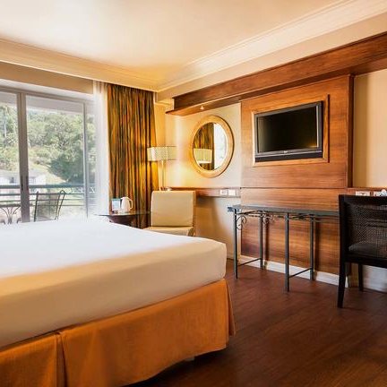 Ein modernes Hotelzimmer mit einem großen Bett, einem Schreibtisch und einem Balkon mit Blick auf die Natur.