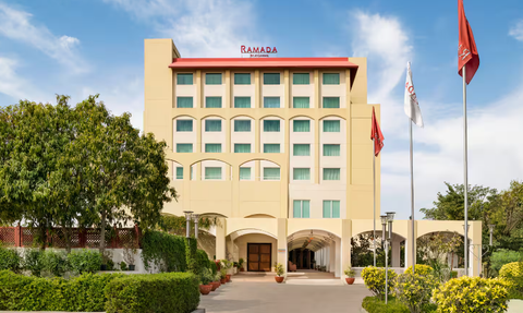 Das Ramada Hotel in Jaipur präsentiert sich mit einer modernen Fassade und einem einladenden Eingangsbereich, umgeben von Grün.