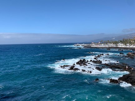 Ein atemberaubender Blick auf das tiefblaue Meer, das sanft gegen die schwarzen Felsen brandet, unter einem strahlend blauen Himmel.