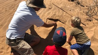 Ein Mann und zwei Kinder sitzen im Sand - Namibia Familienurlaub