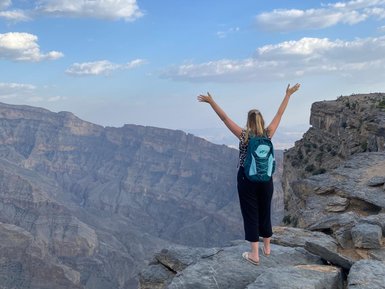 Frau steht auf einem Felsen und genießt die Aussicht über die Schluchten des Jebel Shams – Oman mit Kindern