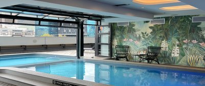 Ein eleganter Innenpool mit glattem Wasser, umgeben von einer tropischen Wandmalerei und modernen Möbeln.