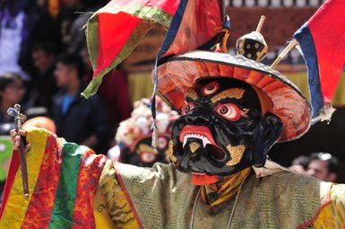 Ein Tänzer in einem beeindruckenden schwarzen Maskenkostüm mit leuchtenden Farben und einem großen Hut führt einen traditionellen Tanz auf.