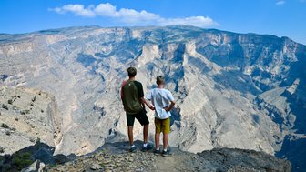Teenager und Kind blicken gemeinsam auf die atemberaubende Schluchtlandschaft des Jebel Shams – Oman mit Kindern