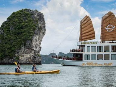 Zwei Kajakfahrer paddeln entspannt in einer ruhigen Bucht, während ein prächtiges Kreuzfahrtschiff im Hintergrund liegt.