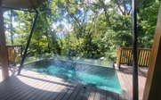 Ein glasklarer Pool schimmert inmitten üppiger, grüner Bäume und Pflanzen, die eine ruhige, tropische Atmosphäre schaffen.