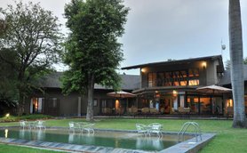 Ein modernes Lodge-Gebäude mit einem einladenden Pool und gemütlichen Sitzbereichen im Freien, umgeben von üppigem Grün.