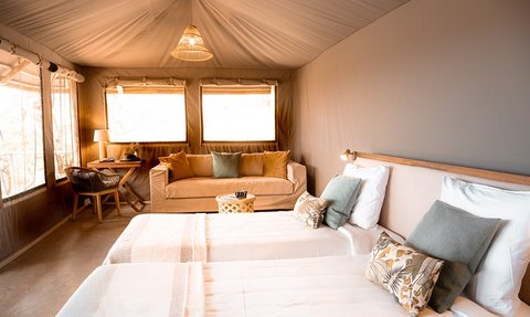 Ein stilvolles Zeltzimmer mit zwei Einzelbetten, einem gemütlichen Sofa und großen Fenstern, die viel Licht hereinlassen.