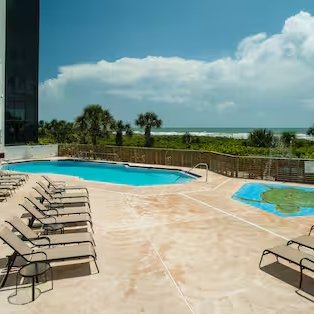 Ein einladender Poolbereich mit Liegen, umgeben von Palmen und Blick auf den Ozean unter einem strahlend blauen Himmel.
