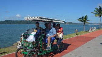 Eine Gruppe von fünf Personen sitzt in einem grünen Fahrrad-Rikschawagen am Amador Causeway in Panama City.