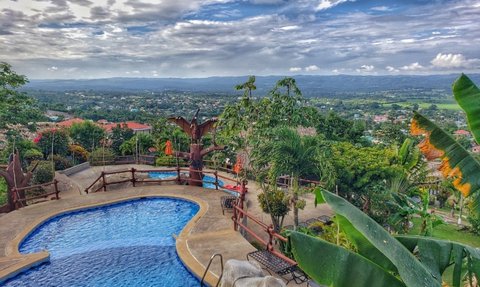 Ein atemberaubender Blick auf einen Pool, umgeben von üppigem Grün und einer malerischen Landschaft unter einem bewölkten Himmel.