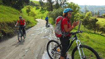 Eine Gruppe von Mountainbikern fährt auf einem schmalen, schlammigen Weg durch eine grüne Landschaft.