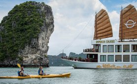 Zwei Kajakfahrer paddeln entspannt in einer ruhigen Bucht, während ein prächtiges Kreuzfahrtschiff im Hintergrund liegt.