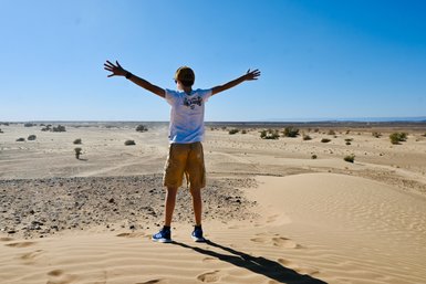 Ein Junge steht mit ausgebreiteten Armen in der Wüste und genießt die Weite der Landschaft.