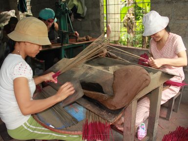 Zwei Frauen arbeiten in einer Werkstatt, während sie kunstvoll Räucherstäbchen aus rotem Material herstellen.