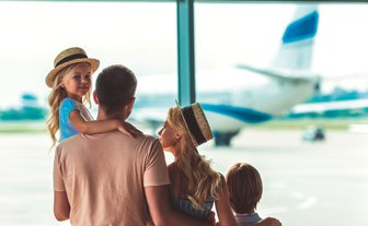 Eine Familie steht am Flughafen und beobachtet ein Flugzeug, während das kleine Mädchen auf dem Arm des Vaters sitzt.