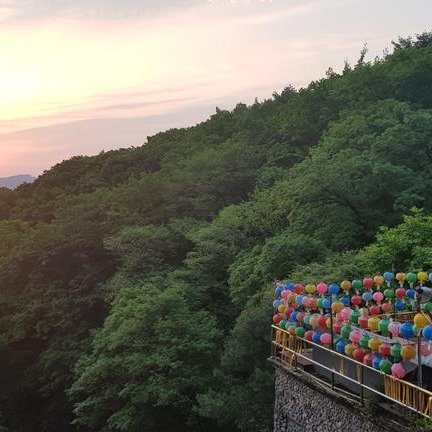 Eine Gruppe von Menschen steht auf einer Terrasse, umgeben von bunten Luftballons, während die Sonne hinter den Bergen untergeht.