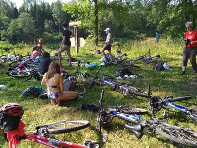Eine Gruppe von Radfahrern macht eine Pause im Grünen, umgeben von Fahrrädern und Natur, während sie sich entspannen.