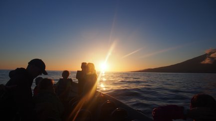 Eine Gruppe von Menschen auf einem Boot beobachtet den Sonnenuntergang über dem ruhigen Wasser des Ozeans.