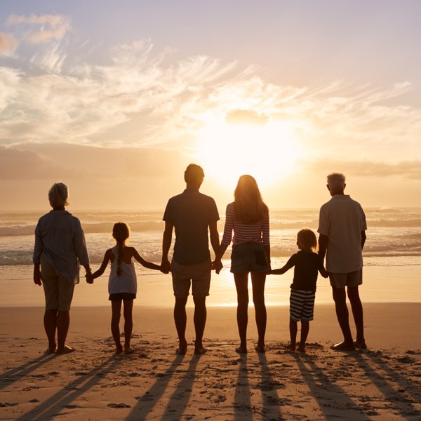 Eine mehrgenerationale Familie steht am Strand, Hand in Hand, während die Sonne am Horizont untergeht.