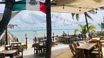 Ein einladendes Restaurant am Strand mit Holztischen und Stühlen, umgeben von Palmen und einer sanften Meeresbrise.