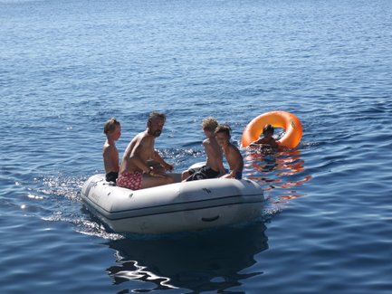 Eine Gruppe von Kindern und einem Erwachsenen fährt in einem Gummiboot auf dem ruhigen blauen Wasser des Meeres.