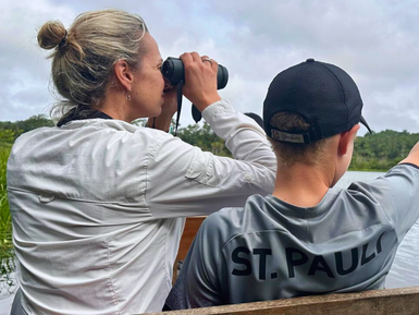 Eine Frau mit blonden Haaren beobachtet mit einem Fernglas die Umgebung, während ein Junge auf das Wasser zeigt.