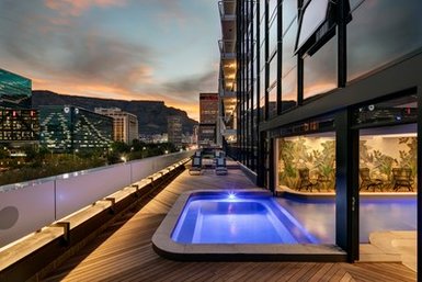 Ein eleganter Balkon mit einem kleinen Pool, umgeben von modernen Gebäuden und einer atemberaubenden Abendkulisse.