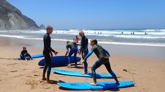 Eine Gruppe von Surfschülern übt auf blauen Surfbrettern am Strand, während die Wellen sanft an den Ufer schlagen.