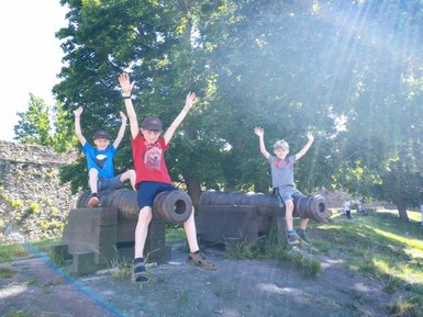 Drei fröhliche Kinder sitzen auf Kanonen und heben die Hände in die Luft, um ihre Freude auszudrücken.