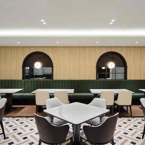 Ein eleganter Restaurantbereich mit hellen Tischen, stilvollen Stühlen und einer gemütlichen grünen Bank im Hintergrund.