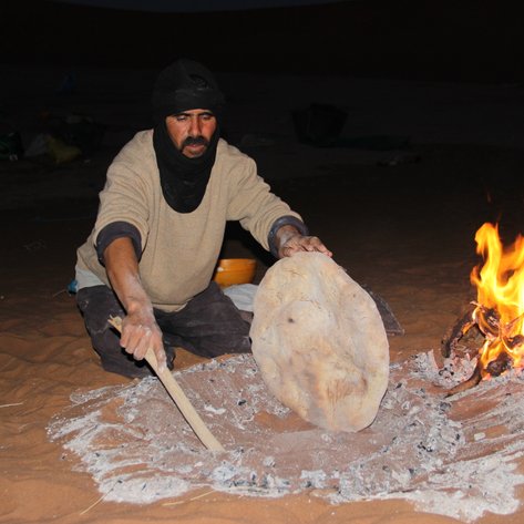 Beduine backt traditionelles Fladenbrot direkt auf dem Wüstensand – Marokko Familienreise