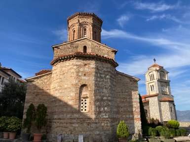 Die alte Kirche mit einem markanten, runden Turm und einem hohen Glockenturm steht unter einem strahlend blauen Himmel.