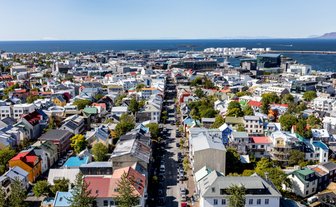 Ein Blick auf Reykjavik zeigt bunte Häuser und eine belebte Straße, die zum Hafen führt, unter strahlend blauem Himmel.