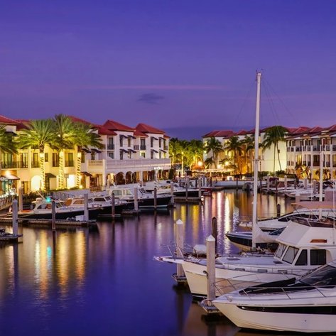 Ein malerischer Blick auf den Yachthafen bei Dämmerung, umgeben von eleganten Gebäuden und Palmen, die sanft im Wind wiegen.