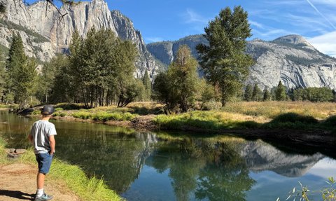 Ein Junge steht am Ufer eines ruhigen Gewässers und betrachtet die majestätischen Berge im Hintergrund.