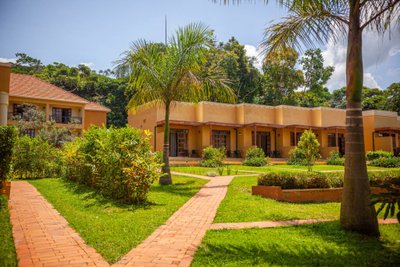 Eine sonnige Landschaft mit einem Lodge-Gebäude, umgeben von üppigem Grün und gepflegten Wegen aus roten Ziegeln.