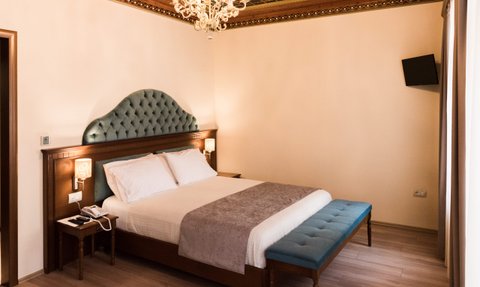 Ein elegantes Hotelzimmer mit einem großen, gepolsterten Bett und einem blauen Hocker am Fußende, umgeben von sanften Farben.