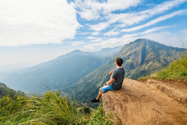 Teenager sitzt auf einem Felsen und blickt auf die grüne Berglandschaft bei Ella – Sri Lanka Familienreise