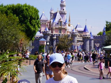 Zwei Kinder stehen vor dem Disneyland-Schloss, umgeben von fröhlichen Besuchern und üppigem Grün.