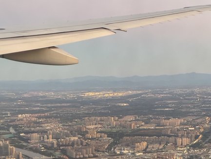 Der Blick aus dem Flugzeug zeigt eine weitläufige Stadtlandschaft mit vielen Hochhäusern und einem Fluss im Vordergrund.