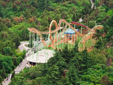Ein aufregender Freizeitpark mit einer bunten Achterbahn, umgeben von üppigem Grün und vielen Besuchern auf den Wegen.