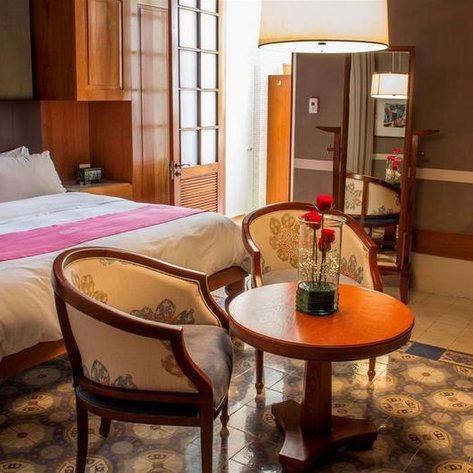 Ein elegantes Hotelzimmer mit einem großen Bett, einem runden Tisch und zwei Stühlen, dekoriert mit frischen Blumen.