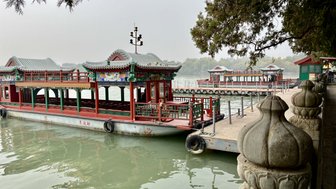 Ein traditionelles chinesisches Boot liegt am Ufer eines ruhigen Gewässers, umgeben von malerischen Pavillons und Bäumen.