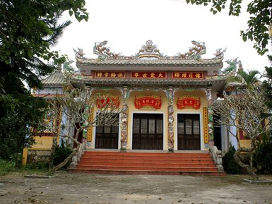 Ein traditionelles Gebäude mit kunstvollen Drachenverzierungen und roten Schriftzeichen, umgeben von Bäumen und Pflanzen.