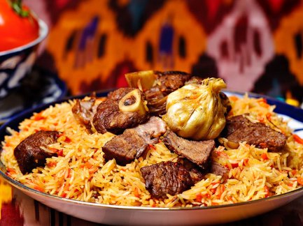 Ein Teller mit duftendem Plov, der mit zartem Fleisch und aromatischem Reis garniert ist, vor einem bunten Hintergrund.