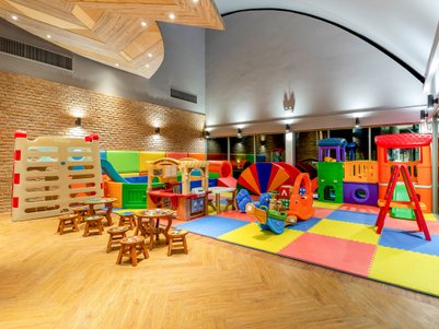 Ein bunter Spielbereich für Kinder mit verschiedenen Spielgeräten, darunter Rutschen, Tische und Spielzeugautos.