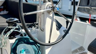 Das Steuerrad einer Yacht steht im Vordergrund, während ein Rucksack mit dem Aufdruck 'For Family Reisen' daneben liegt.