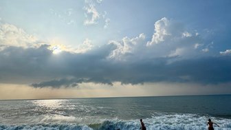 Zwei Kinder laufen am Strand entlang, während die Wellen sanft an den Ufer schlagen und der Himmel bewölkt ist.